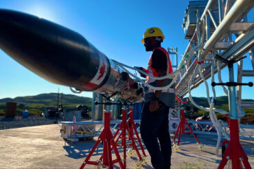 A technician in a hardhat and high-res vest stands next to a Nordspace rocket