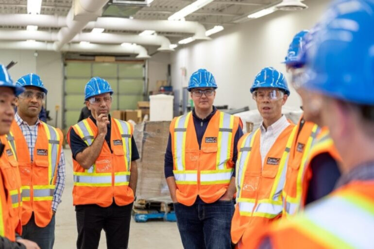 A group of approximately 6 men stand in safety vests and hard hats.