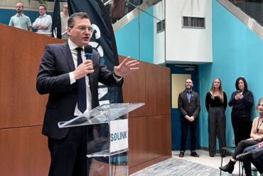 Evan Solomon speaks into a microphone while gesturing his hand.