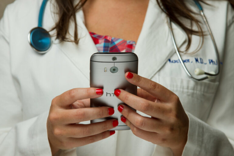 A close-up of a doctor's hands using a cell phone.