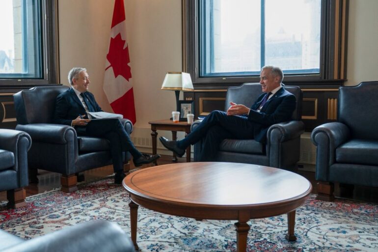 Canada's Minister of Finance, Francois-Philippe Champagne, and Prime Minister Mark Carney face eachother on opposite couches, laughing.