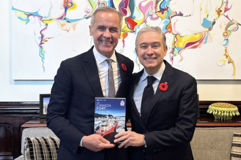 Mark Carney and François-Philippe Champagne stand together, smiling, hold a copy of Budget 2025.