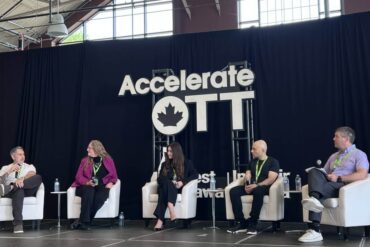 Several people sit on stage under an AccelerateOTT sign.