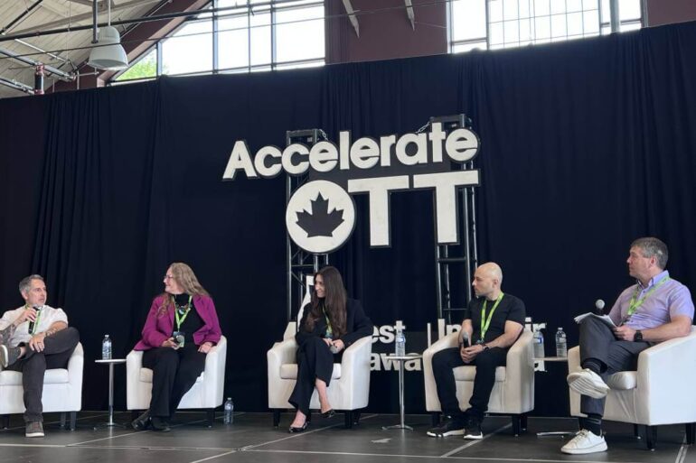 Several people sit on stage under an AccelerateOTT sign.