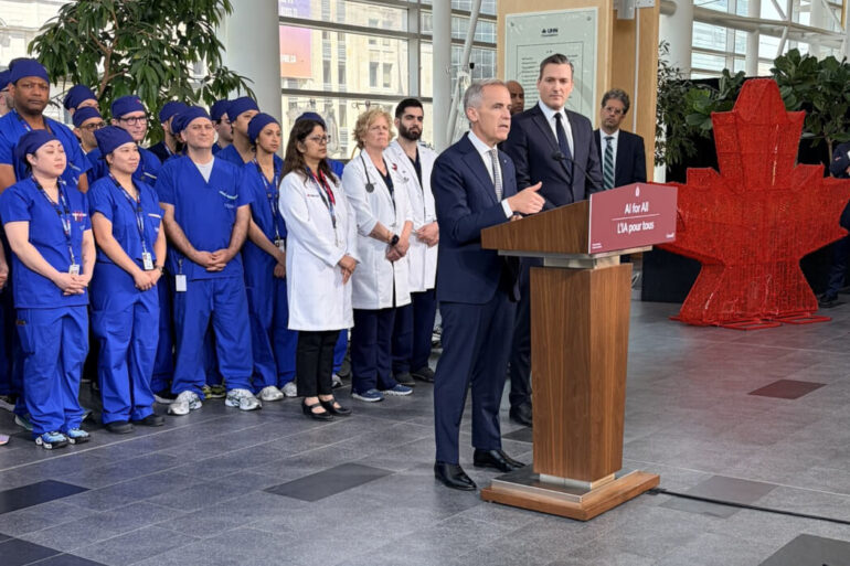 Mark Carney and Evan Solomon standing at a podium in front of a group of people.