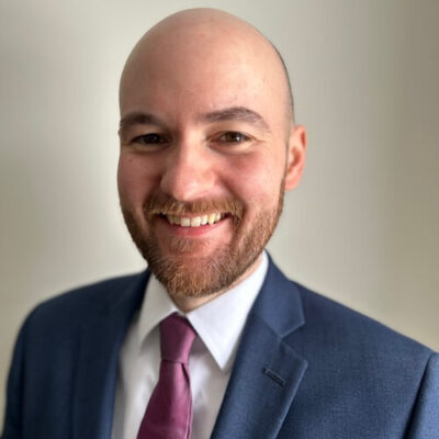 A photo of a man in a suit smiling at the camera.