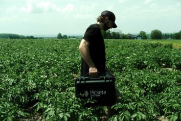 A man in the middle of a planted crop holding a Picketa briefcase.